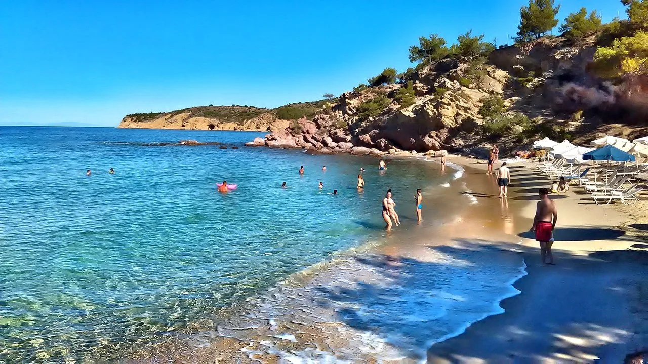 Aerial view of Marble Beach on Thassos island with turquoise waters, white pebbles, and lush green pine trees under a clear blue sky